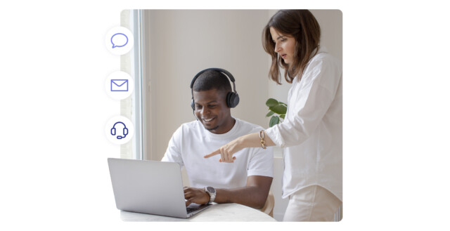 Freundlicher Support-Mitarbeiter mit Headset am Laptop, Kollege zeigt auf den Bildschirm; links Symbole für Chat, E-Mail und Anrufe